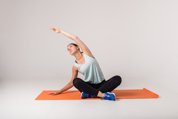 Beautiful woman performs warm-up on a Mat on a white