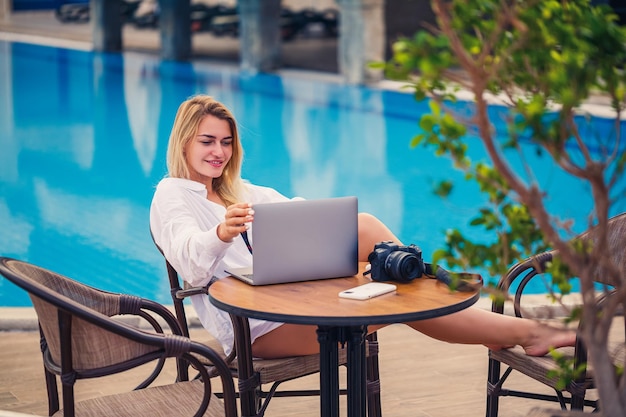 Bella donna fotografa blogger in vacanza che lavora con il laptop in piscina lavoro a distanza freelance