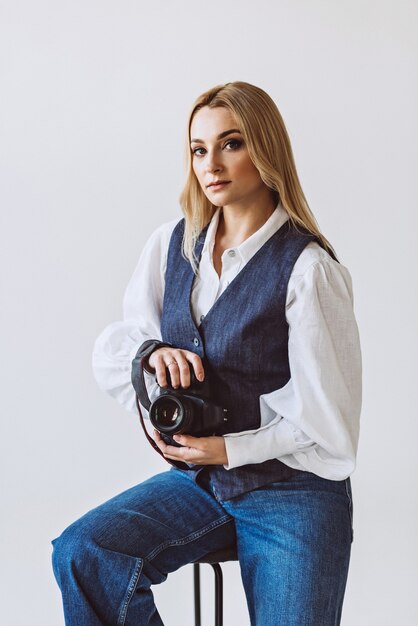 A beautiful woman photographer in a denim casual outfit and a white blouse with voluminous sleeves with a camera in her hands. Hobbies. Soft selective focus.