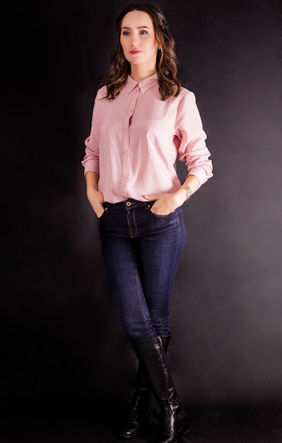 Beautiful woman in a pink blouse and jeans stands on a black background