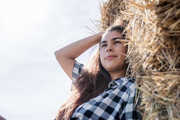 Красивая женщина в клетчатой рубашке и ковбойской шляпе отдыхает на стоге сена