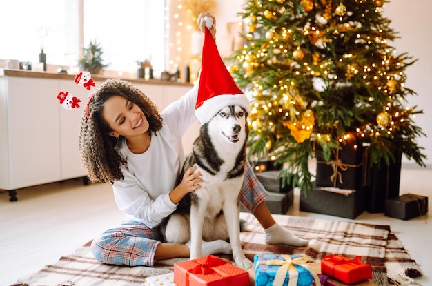 Beautiful woman playing and having fun with her dog while sitting near the christmas tree