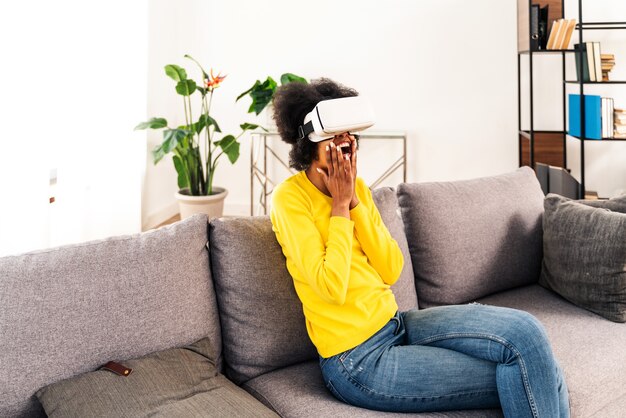 Bella donna che gioca a casa con l'auricolare vr - donna nera sdraiata sul divano mentre interagisce con la tecnologia della realtà aumentata augment