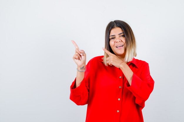 Beautiful woman pointing at upper left corner in red blouse and looking cheery , front view.