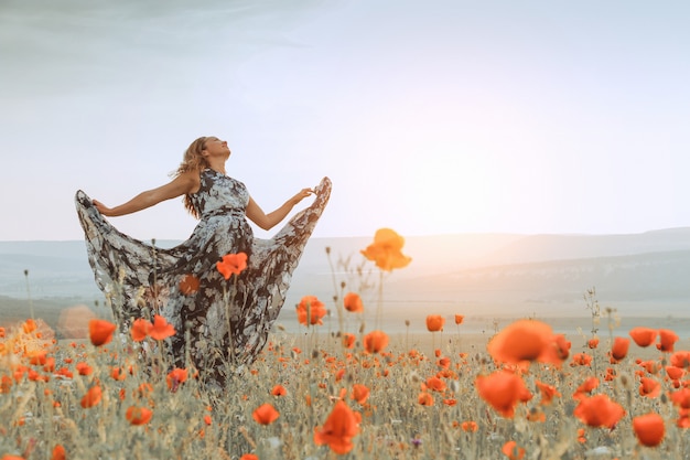 Foto bella donna in un campo di papaveri al tramonto.