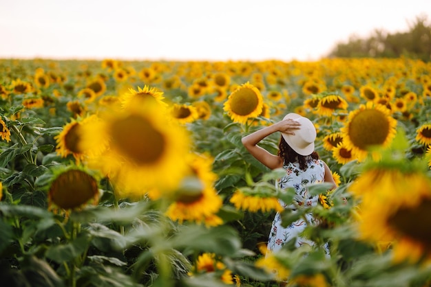 Beautiful woman posing in a field of sunflowers in a dress and hat Fashion lifestyle concept