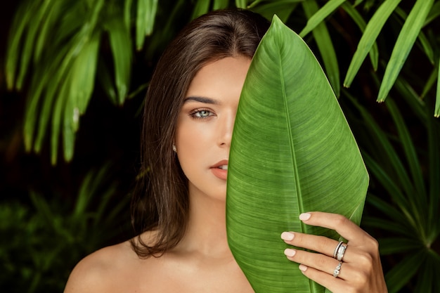 Beautiful woman posing near green leaves