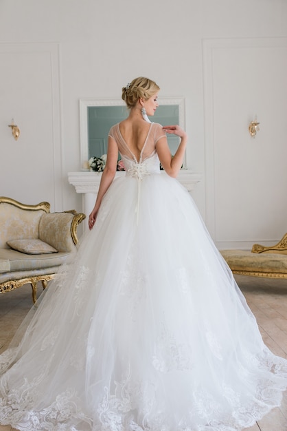 The beautiful woman posing in a wedding dress in luxury interior