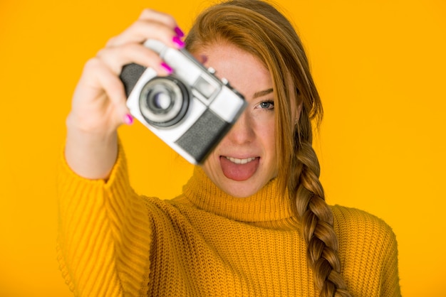 Beautiful woman posing with camera on orange wall