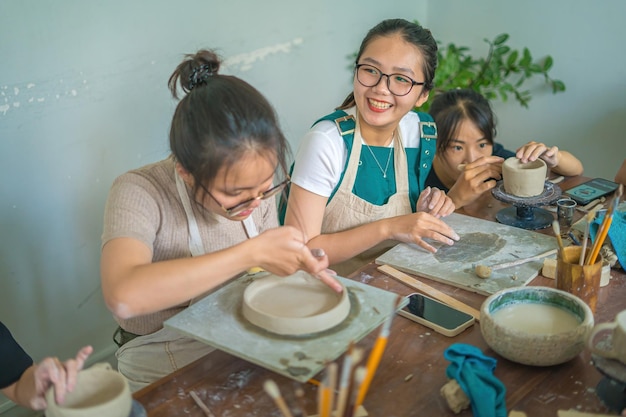 Beautiful woman potter working on potters wheel making ceramic pot from clay in pottery workshop Focus hand young woman attaching clay product part to future ceramic product Pottery workshop