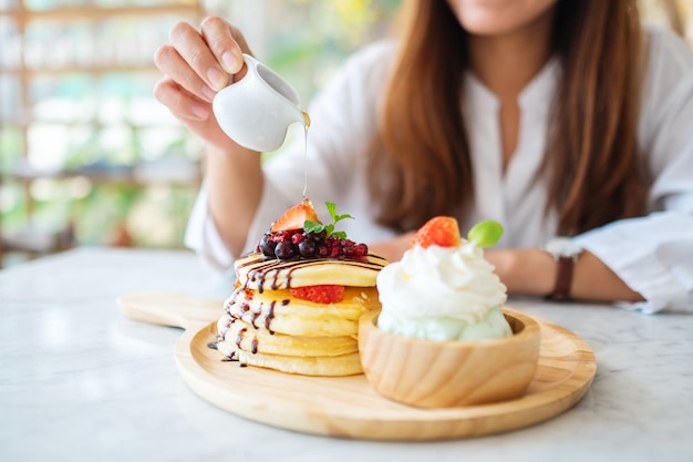 Photo a beautiful woman pouring honey into a piece of mixed berries pancakes with ice cream and whipped cream