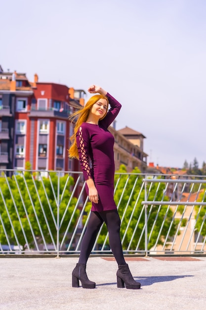 Beautiful woman in purple dress and black boots enjoying in a park in the city, posing looking at camera