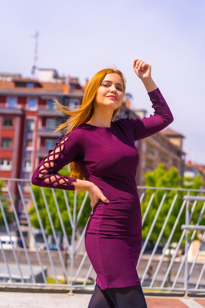 Beautiful woman in purple dress and black boots enjoying in a park in the city, posing looking at camera