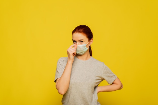 Beautiful woman put on medical mask on a yellow wall. Coronavirus and covid-19 concept.