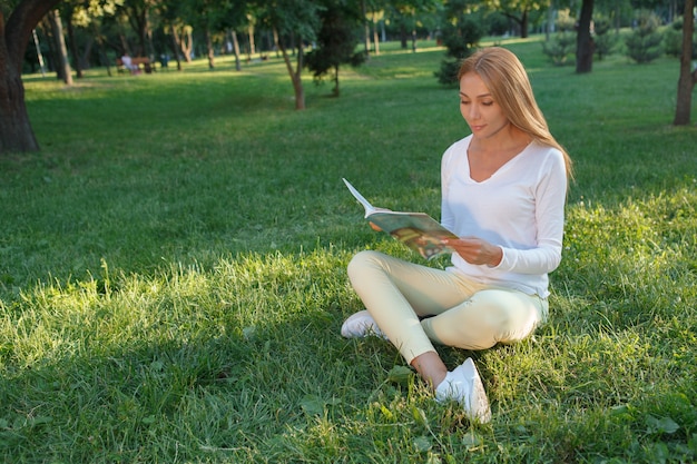 本を読んで、草の上に座って、スペースをコピーする美しい女性