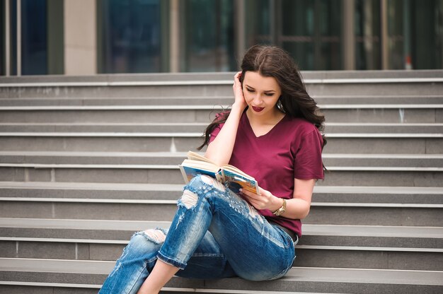 Beautiful woman reading a book on the steps of the building