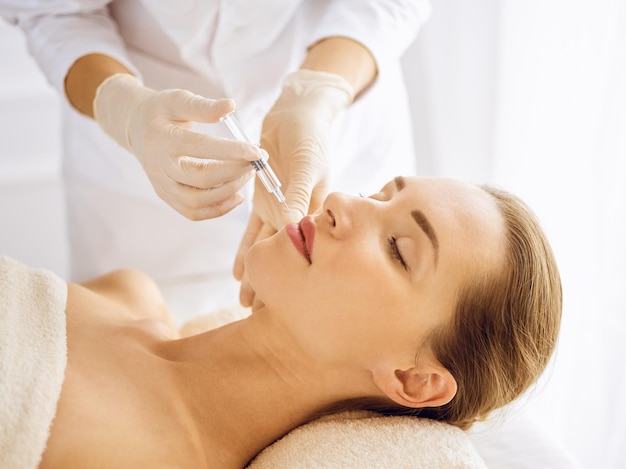 Beautiful woman receiving beauty injections with closed eyes. Beautician doctor hands doing beauty procedure to female face with syringe. Cosmetic medicine and surgery concept