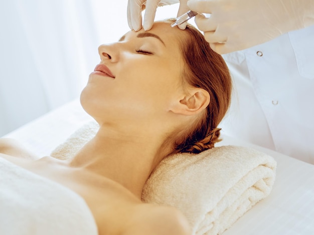 Beautiful woman receiving beauty injections with closed eyes in medical center. Beautician doctor hands doing beauty procedure to female face with syringe. Cosmetic medicine and surgery concept