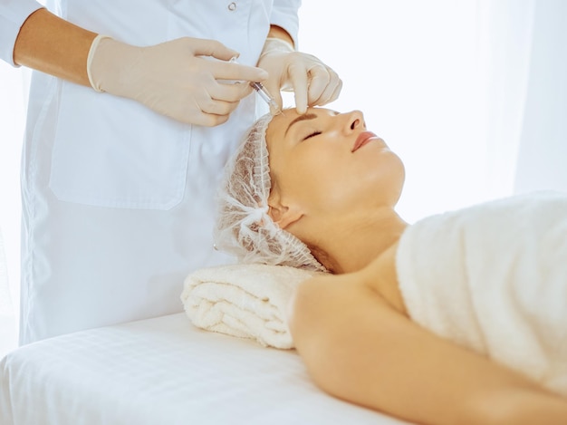 Beautiful woman receiving beauty injections with closed eyes in medical center. Beautician doctor hands doing beauty procedure to female face with syringe. Cosmetic medicine and surgery concept