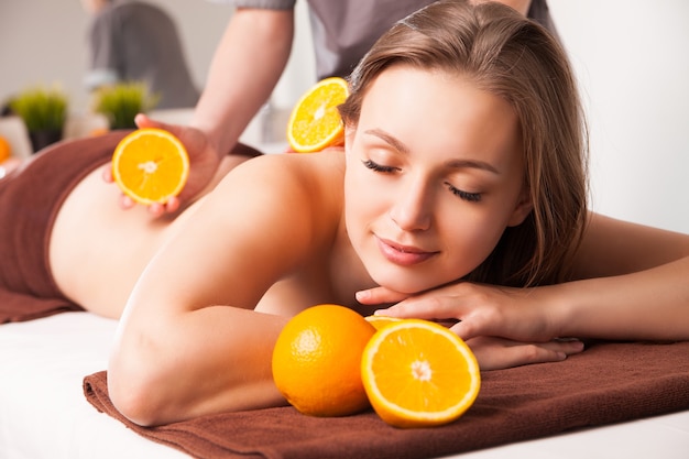 Beautiful woman receiving spa procedures with oranges in spa salon