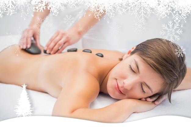 Beautiful woman receiving stone massage at spa center against fir tree forest and snowflakes