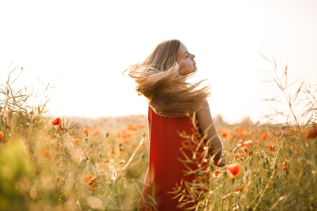 Bella donna in un vestito rosso in un campo di papaveri in fiore. messa a fuoco selettiva