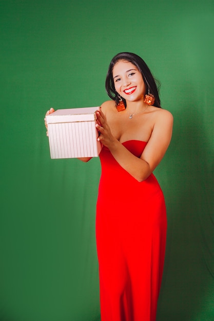 贈り物を保持している赤いドレスの美しい女性。緑の背景で撮影したスタジオ..クリスマス。