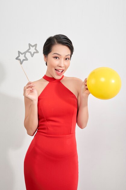 Beautiful woman in red dress is posing with paper eyeglasses in hand balloon over white background