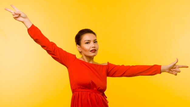 Beautiful woman in red dress pointing finger on yellow background