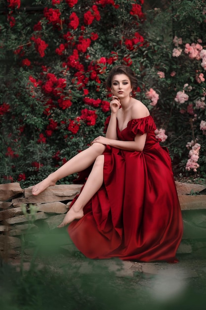 Beautiful woman in red dress walking in the garden full of roses