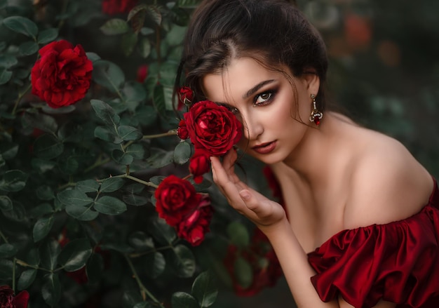 Beautiful woman in red dress walking in the garden full of roses