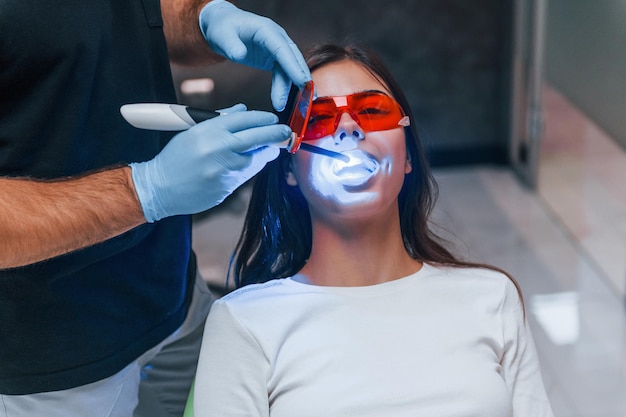 Foto la bella donna con gli occhiali protettivi rossi ha una visita nella clinica del dentista. concezione della stomatologia.