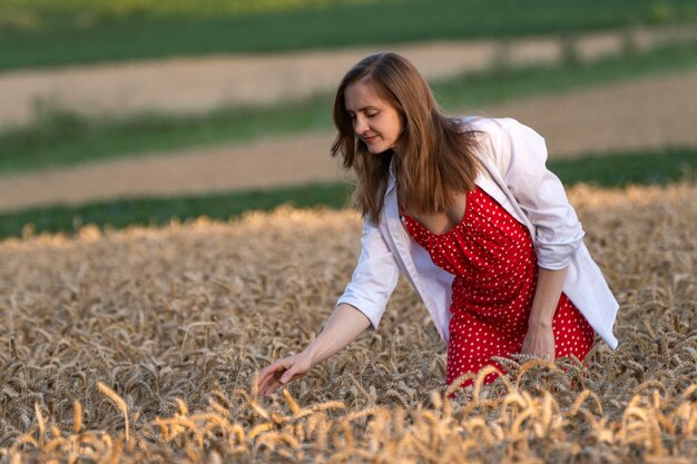 Beautiful woman in red sundress and white shirt in the middle of wheat field with ripe ears Agriculture Bread harvest