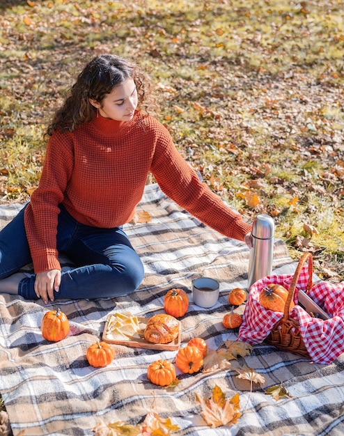 秋の森のピクニックで赤いセーターの美しい女性