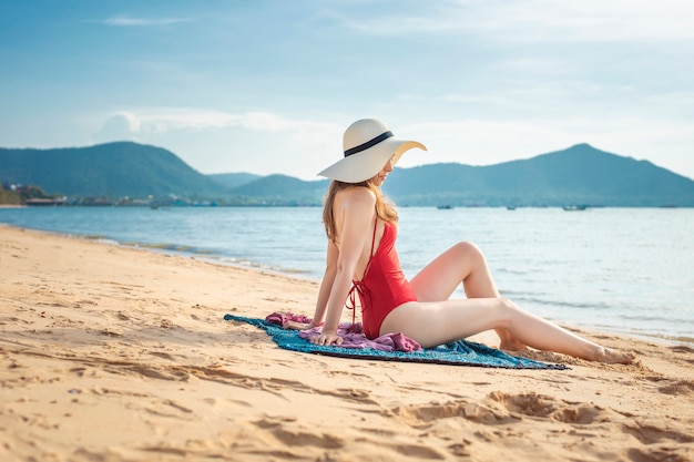 La bella donna in costume da bagno rosso sta sedendosi sulla spiaggia