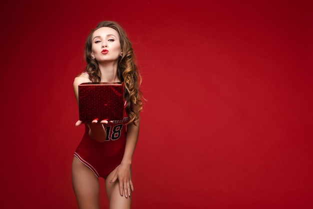 A beautiful woman in a red swimsuit with bright makeup and red lips with a gift in her hands