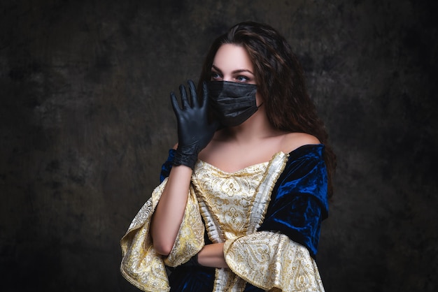 Bella donna in abito rinascimentale, maschera facciale e guanti, coronavirus, concetto di protezione covid-19.