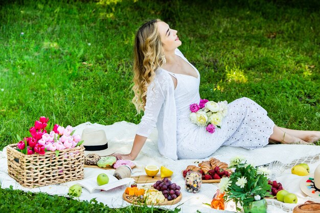 Beautiful woman resting in park sitting on a picnic blanket with fruits and wine