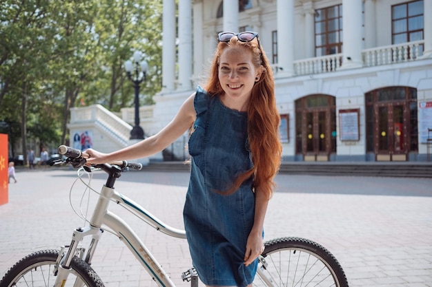 Bella donna in bicicletta stile di vita e salute in città una giovane donna allegra dai capelli rossi si diverte a passeggiare per la città