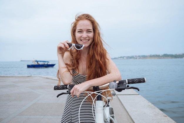 Beautiful woman riding on bike Lifestyle and health in the city Cheerful redhaired young woman gets pleasure from walking around the city