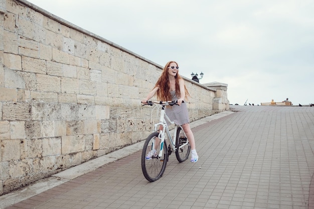 Beautiful woman riding on bike Lifestyle and health in the city Cheerful redhaired young woman gets pleasure from walking around the city