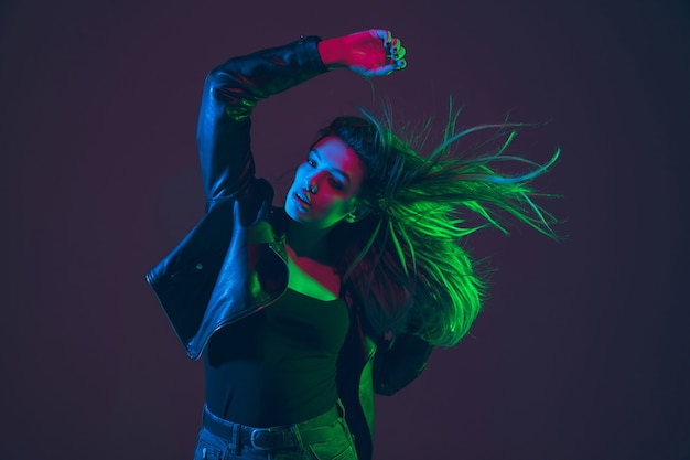 Beautiful woman's portrait with blowing, flying hair on dark studio background in colorful green, red, blue neon light. Concept of human emotions, ad. Trendy colors. Fashion and beauty in motion.