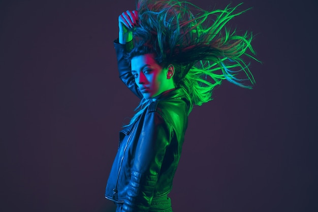 カラフルな緑、赤、青のネオンの光で暗いスタジオの背景に吹く、飛んでいる髪の美しい女性の肖像画。人間の感情の概念、広告。トレンディな色。動きのあるファッションと美しさ。