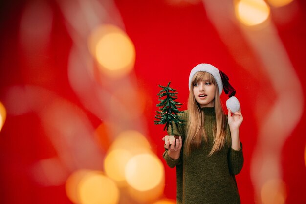 A beautiful woman in a Santa hat holds a small Christmas tree in her hands New year concept