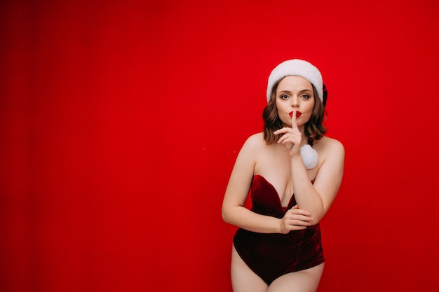 beautiful woman in santa hat and red bodysuit on a red background New year concept