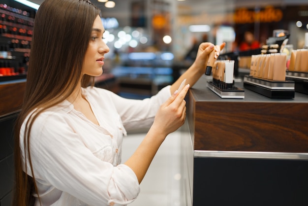 Beautiful woman at the shelf in cosmetics store, side view. Buyer at the showcase in luxury beauty shop salon, female customer in fashion market