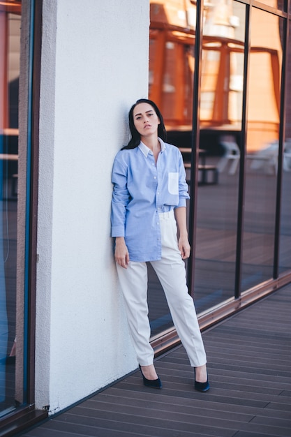 A beautiful woman in a shirt and pants is standing by the mirror