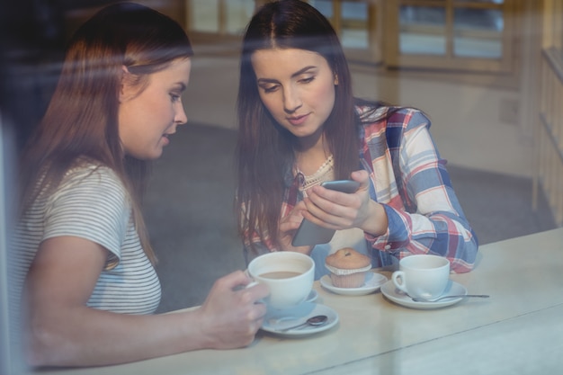 Beautiful woman showing cellphone to friend at cafe