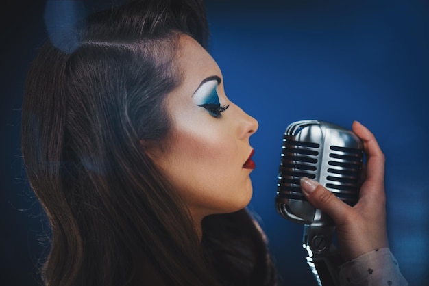 Una bella cantante donna con capelli e trucco retrò alla moda tiene in mano un microfono vintage con supporto pronto a cantare.