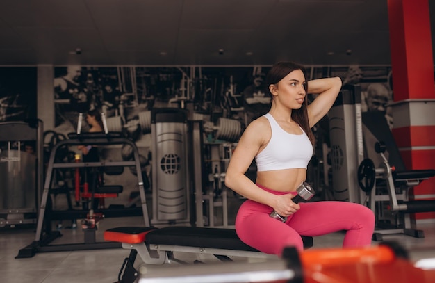 A beautiful woman sits on a bench The coach is resting after a productive roundabout Female athlete in sportswear in the gym